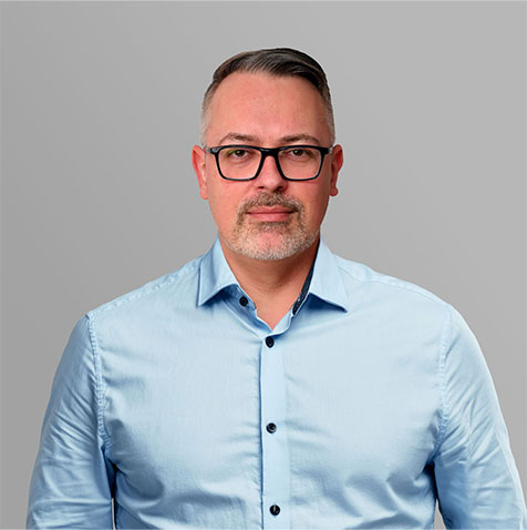 Portr&auml;t eines Ansprechpartners mit Brille und blauem Hemd vor grauem Hintergrund