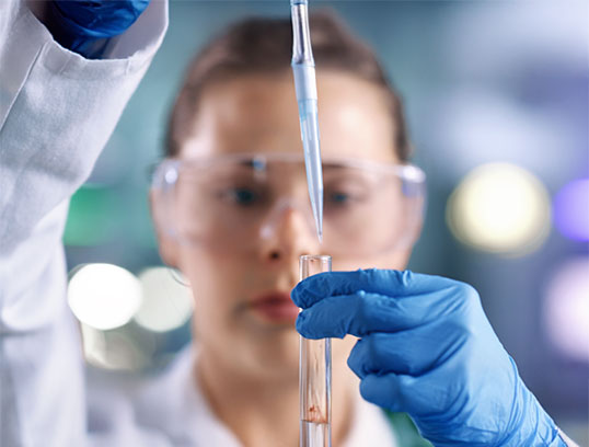Wissenschaftlerin pipettiert Fl&uuml;ssigkeit ins Reagenzglas mit Schutzkleidung